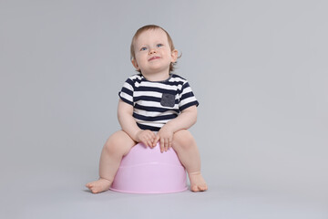 Little child sitting on baby potty against light grey background