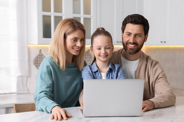 Happy family with laptop at white table indoors