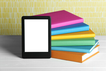 Portable e-book reader and stack of books on white wooden table