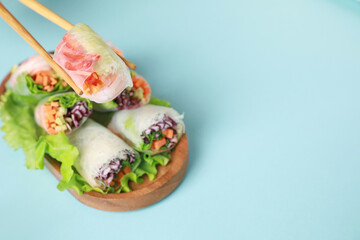 Holding delicious spring roll with chopsticks on light blue background, closeup. Space for text
