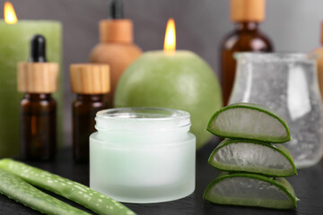 Jar of natural gel and aloe vera leaves near cosmetic products on black table, closeup