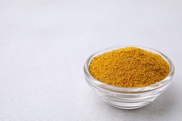 Glass bowl with curry powder on white table, closeup. Space for text