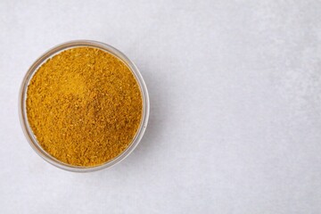 Glass bowl with curry powder on white table, top view. Space for text