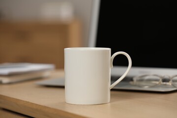 White ceramic mug and laptop on wooden table at workplace