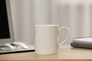 White ceramic mug, glasses and laptop on wooden table at workplace