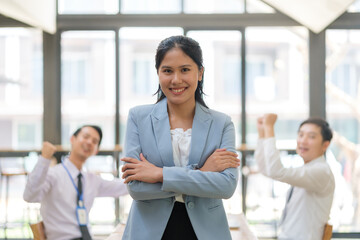 Fototapeta premium Successful businesswoman standing with arms crossed with coworkers cheering or congratulation with professional achievement.