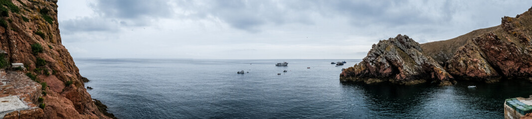 Naklejka premium Panoramic view of the coast of the Berlenga Islands in the Atlantic Ocean of Portugal. Cloudy landscape of the Iberian Peninsula. Fishing boats in the water.