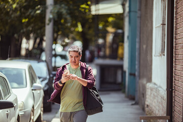 Middle aged man walking home from the gym on the sidewalk of a city street