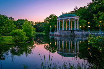 Bandstand Pavillion scenic spot landscape illuminated at sunset with water reflections on Roosevelt Lake at Roger Williams Park in Providence, Rhode Island - obrazy, fototapety, plakaty