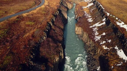 Drone shot of gullfoss river cascade, majestic water stream flowing between colorful snowy hills and fields. Icelandic nature and landscape near waterfall. Slow motion. - Powered by Adobe