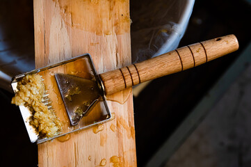A honey uncapping tool with beeswax on it sitting on a wood board