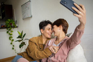 Same sex couple at home spending time. Latin Lgbtq couple using mobile phone to take a selfie 