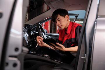 One young expert Asian male automotive mechanic technician checking a maintenance list with tablet in car interior at garage. Vehicle service fix and repair works, industrial occupation business jobs.