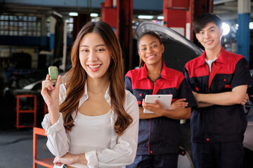 Young Asian female customer shows car key with automotive mechanic workers, happy smile in quality...