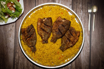 Fried fish with rice in a plate on a wooden table With Green Salad Plate beside it and spoon and fork 