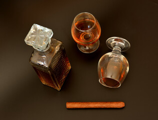 Two glass goblets, a crystal decanter of cognac and a Cuban cigar on a black background.