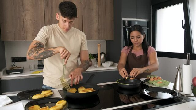 Two young latin people cooking llapingachos and eggs in a pan at kitchen.