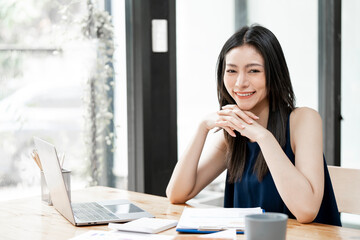 Charming Asian businesswoman working with a laptop at the office. Looking at camera.