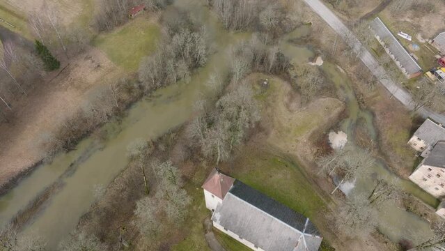 Aerial birdseye view of high water in springtime, flood, Durbe river (Latvia), Cirava city, brown and muddy water, sunny day, wide drone shot moving forward over the rooftops
