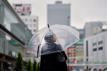 雨の歩道を歩くビジネスウーマンの後ろ姿