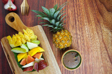Sliced Fruit Salad, in Indonesia known as Rujak Buah or Lutis or Lotis. Served with Spicy Brown Sugar sauce and Ground Peanuts in a plate on wood background
