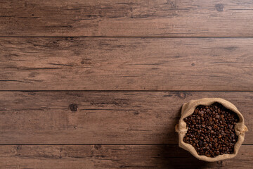 The many coffee beans are placed around on a wooden table in a warm, light atmosphere, on dark background, with copy space.