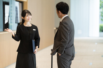 A scene of a woman in the hospitality industry giving information at a reception desk in a hotel during a business or travel trip in Japan or Asia Wide-angle full body