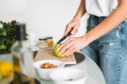 Young slim woman in white t-shirt and blue jeans cooking healthy food with apple in kitchen at home