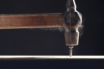An old hammer hits a nail close-up on dark background. Dust rises from the impact. Carpentry...