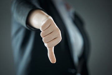 Female thumb down close-up on the background of suit in blur. Business concept. - obrazy, fototapety, plakaty