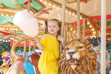 Fototapeta na wymiar Adorable little girl in summer yellow dress at amusement park having a ride on the merry-go-round