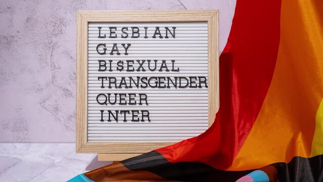 Stop motion LGBTQIA description frame on Rainbow LGBTQIA flag made from silk material. LESBIAN, GAY, BISEXUAL, TRANSGENDER, QUEER, INTERSEX, ASEXUAL. Symbol of LGBTQ pride month. Equal rights. Peace