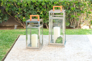two candles are displayed inside the transparent glass lanterns on concrete slabs, in the garden of...