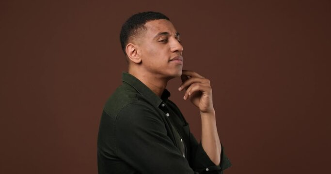 Pensive african american guy pointing at camera and talking to someone standing over brown studio background
