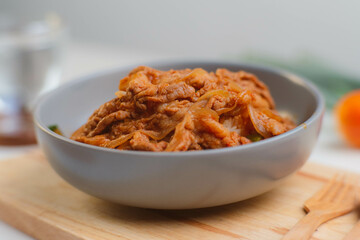 Fried kimchi with kurobuta pork on cooked rice in a bowl on wooden background. Korean food