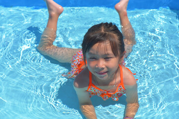 Happy little girl swimming pool on a hot summer day. Kids learn to swim. Child water toys. Children play in tropical resorts. Family beach vacation.