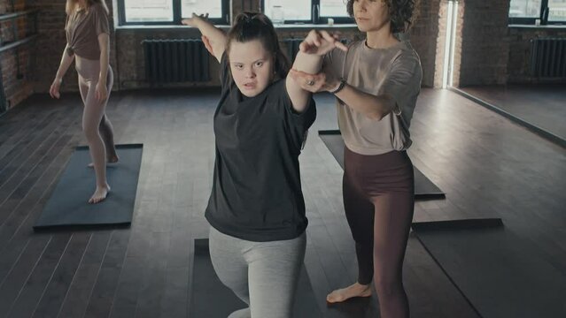 Tilt Up Slow Motion Of Professional Yoga Trainer Correcting Warrior Pose Young Woman With Disability Doing