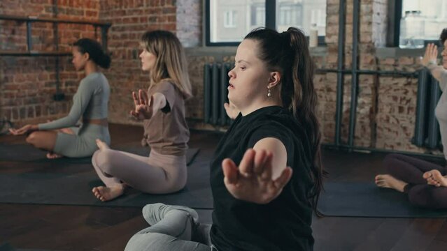 Selective focus shot of modern yoga trainer with Down syndrome working with group of women in loft room