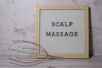 Scalp massager for home with letter board SCALP MASSAGE text. Close up of scalp massaging brush for hair growing routine. Anti stress acupuncture metal octopus tool equipment. Manual device for home - obrazy, fototapety, plakaty