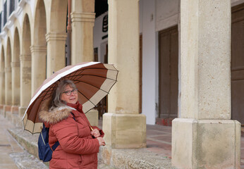 woman with umbrella and backpack looking at the camera standing in front of stone arches