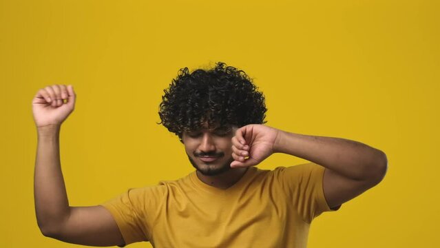 Young indian bearded guy with curly hair wearing t-shirt dancing over orange studio background