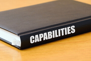 Book with CAPABILITIES inscription lie on the wooden table.