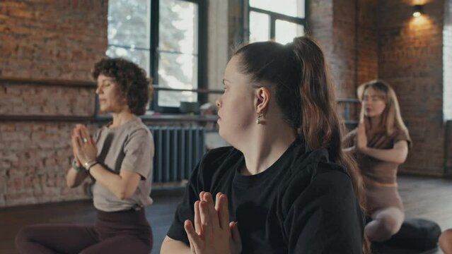 Selective focus shot of modern girl with Down syndrome attending yoga class practicing meditation