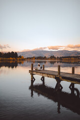 Wide shot of a woman sitting on a pier playing the guitar in Cromwell, New Zealand