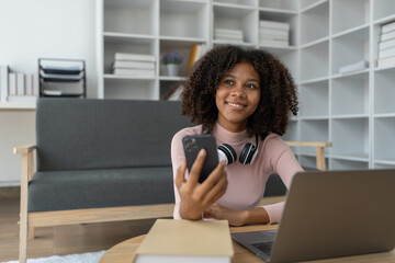 Young African American woman using mobile phone to attend online training Talk while learning via video call on laptop computer. Using headset. E-education, online class, training concept.