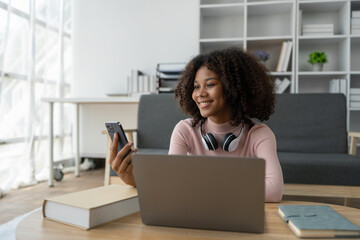 Young African American woman using mobile phone to attend online training Talk while learning via video call on laptop computer. Using headset. E-education, online class, training concept.