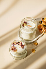 Handmade candle from paraffin and soy wax in glass with wooden wick and dry herbal isolated on pastel beige background. Flat lay, top view, copy space