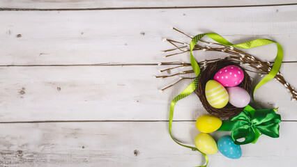 Colorful Easter eggs in the nest with text happy easter on white wooden background. Easter holiday concept, flat lay, top view. Copy space