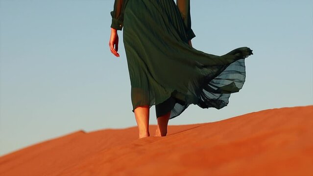 woman in green long dress stands in desert sand dunes background yellow orange sunset