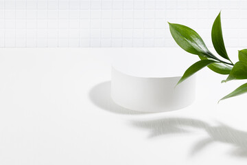Summer abstract white stage with one round podium mockup for presentation cosmetic products, advertising, design in light interior, tiny mosaic tile, fresh tropical green leaves in sunlight, shadow.